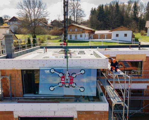 Mit dem Kran werden die großen Glasscheiben für die große Glasfront eines Neubaus in Hanglage zur Montage gehoben.