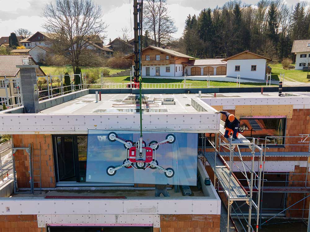 Mit dem Kran werden die großen Glasscheiben für die große Glasfront eines Neubaus in Hanglage zur Montage gehoben.
